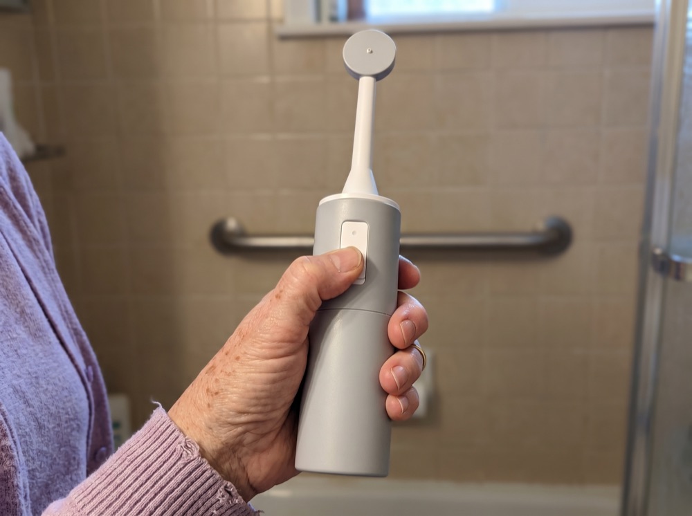 A hand holding the gray handheld bidet, thumb on the button